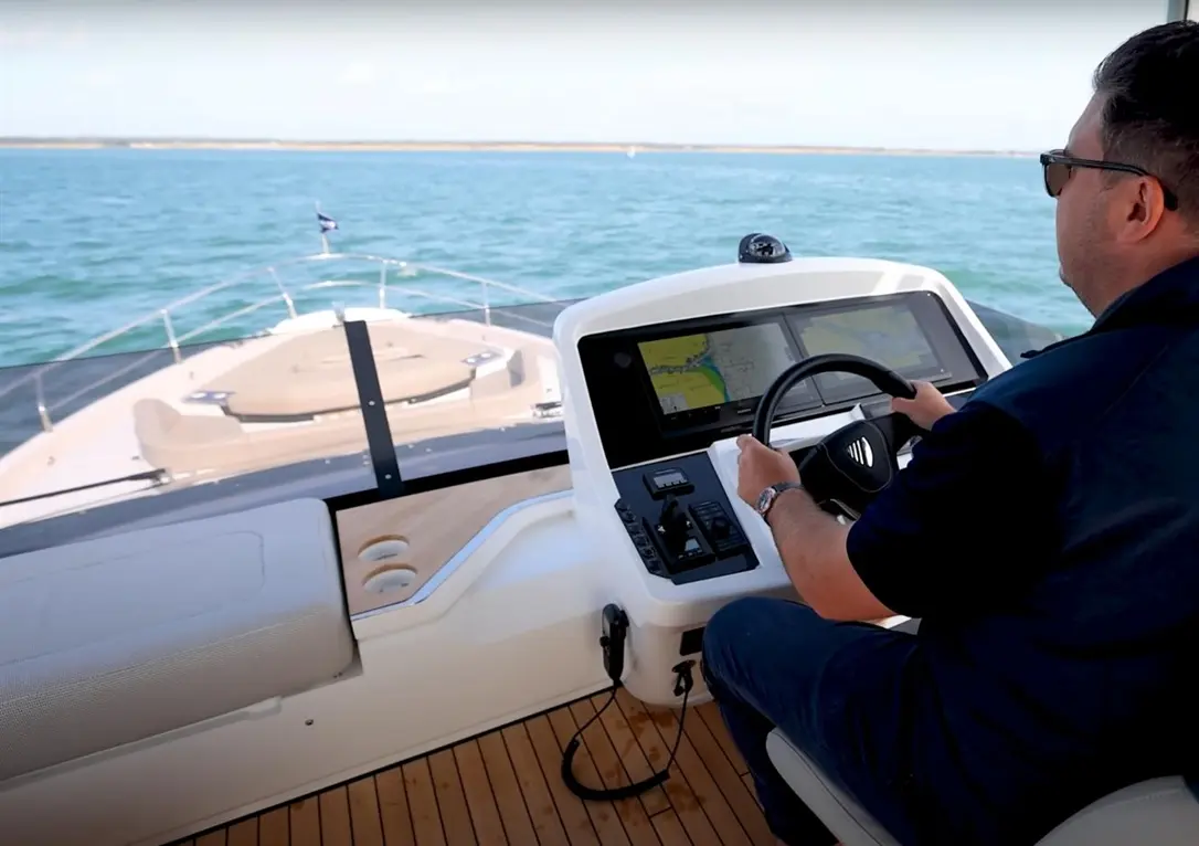 Man steering a motorboat with a chart display, navigating on blue waters, showcasing modern nautical technology.